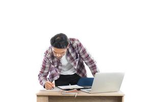 Young businessman  looking and writing on his notepad sitting at his working place isolated on white background.