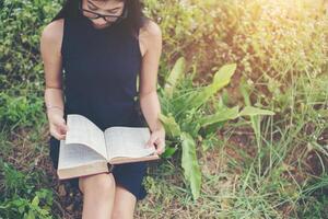 mujer hermosa joven relajada leyendo un libro en el césped con el sol brillando. foto