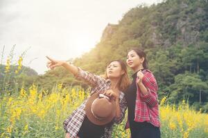 Two hipster women traveling and pointing hands enjoying with flower field together, relaxing good time sunny day. photo