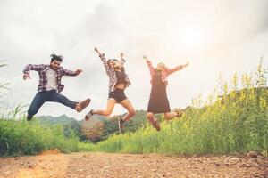 grupo de adolescentes saltando en el campo de flores amarillas, disfrutando de la naturaleza y la brisa fresca contra la montaña detrás. foto