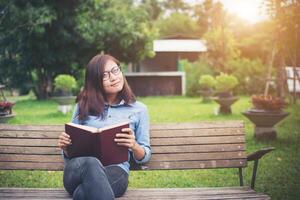 chica encantadora hipster relajándose en el parque mientras lee un libro, disfruta de la naturaleza. foto