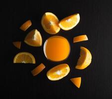 Sliced oranges with glass on black background photo