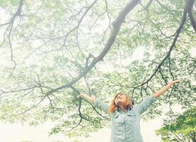 mujer joven abre los brazos de pie en la vegetación de primavera fresca con la cabeza levantada hacia el cielo. foto