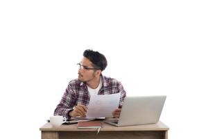 Thoughtful young buisnessman  looking away while sitting at his working place and business chart in hand isolated on white background. photo