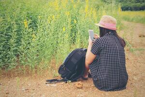 Rear View of a young woman facing at the phone while sitting on a flowers field. photo