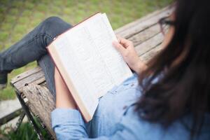 chica encantadora hipster relajándose en el parque mientras lee un libro, disfruta de la naturaleza. foto