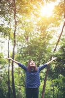 Attractive young woman standing in a forest, hands spread around and enjoy the refreshing natural surroundings. photo