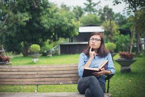 Hipster charming girl thinking something while reading red book in the green park. photo