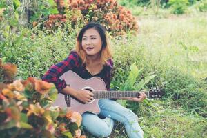 Young beautiful hipster woman playing guitar sitting on grass in the park, Relaxing with nature. photo