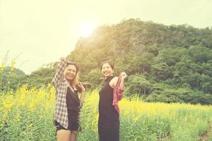 dos mujeres hipster viajando y disfrutando juntas con un campo de flores, relajándose un buen día soleado. foto