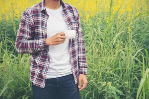 Bearded man with cup of morning coffee walking in the flower field. photo