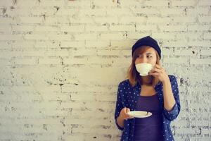 bella mujer bebiendo café sobre fondo de pared de ladrillo blanco foto