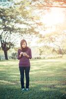 Woman standing alone in park writing text on smartphone photo