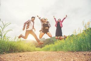 grupo de adolescentes saltando en el campo de flores amarillas, disfrutando de la naturaleza y la brisa fresca contra la montaña detrás. foto