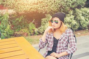 Outdoor portrait of young hipster woman sitting alone at old city cafe and waiting for her boyfriend wearing plaid outfit and  sunglasses. photo