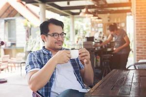 hipster man holding a cup of coffee while sitting at cafe looking away and smile. photo