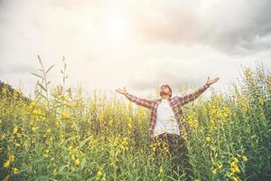 Handsome hipster man standing raising hands in the air in a yellow flower field. photo