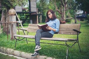 Hipster charming girl relaxing in the park while read book, Enjoy nature around. photo