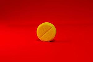 Yellow one pill on a bright red background close-up. Place for your text. Selective focus. photo