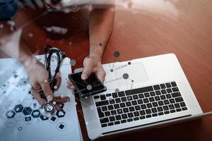 vista superior de la mano del médico que trabaja con una computadora moderna y un teléfono inteligente en un escritorio de madera como concepto médico foto