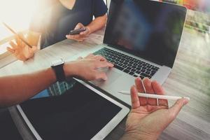 two colleagues interior designer discussing data and blank screen digital tablet and computer laptop with smart phone on wooden desk as concept photo