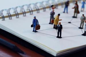 close up of miniature people with social network diagram on open notebook on wooden desk as social media concept photo