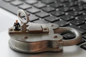 Internet security concept-miniature businessman stand on old key and padlock on laptop computer keyboard photo