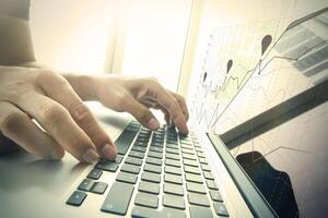 close up of business man hand working on laptop computer with business graph information diagram on wooden desk as concept photo