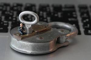 Concepto de seguridad en Internet: empresario en miniatura se para en una llave antigua y candado en el teclado de la computadora portátil foto