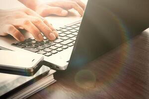 designer hand working with digital tablet and laptop and notebook stack and eye glass on wooden desk in office photo