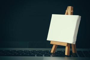 blank canvas and wooden easel on laptop computer as concept photo