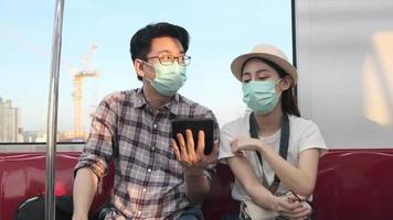 jovem máscara facial casal turistas asiáticos pesquisam informações, encontram locais de viagem pelo mapa do tablet em uma cabine de trem, estilo de vida de viagem de férias de passageiros, transporte casual, viagem de férias na tailândia. video