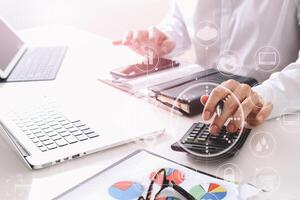 businessman hand working with finances about cost and calculate  and latop with mobile phone on withe desk in modern office photo