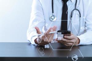 close up of smart medical doctor working with smart phone and stethoscope on dark wooden desk with virtual icon diagram photo