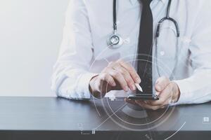 close up of smart medical doctor working with smart phone and stethoscope on dark wooden desk with virtual icon diagram photo