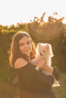 chica morena adolescente con spitz en sus brazos. la niña está feliz con su mascota. foto