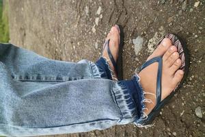 the legs of someone wearing jeans and flip-flops photo