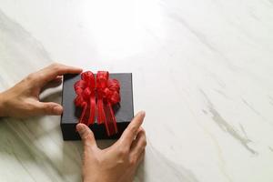 entrega de regalos, mano de hombre sosteniendo una caja de regalo en un gesto de dar sobre fondo de mesa de mármol gris blanco foto