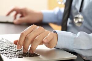 close up of smart medical doctor working with laptop computer and mobile phone and stethoscope on dark wooden desk photo