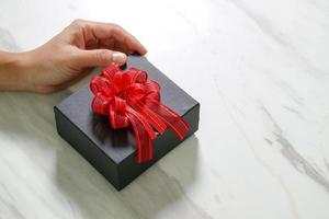 entrega de regalos, mano de hombre sosteniendo una caja de regalo en un gesto de dar sobre fondo de mesa de mármol gris blanco foto