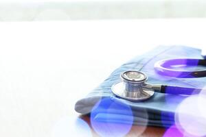 Stethoscope with blue doctor coat on wooden table with shallow DOF evenly matched and background photo