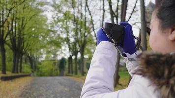 mujer asiática tomando una foto de vista en el parque en otoño. trajes de otoño, buen tiempo, hojas amarillas cayendo en la calle. mucho fondo de árbol, estocolmo, suecia en concepto de otoño video