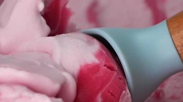 gros plan, crème glacée ramassée avec une cuillère bleue. glace à la viande rose parfumée à la fraise. video