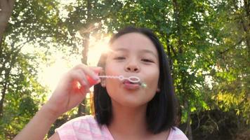 niña asiática que sopla pompas de jabón. feliz niña de asia divirtiéndose y disfrutando del juego al aire libre soplando burbujas de jabón durante el parque del jardín en un día soleado, horario de verano video