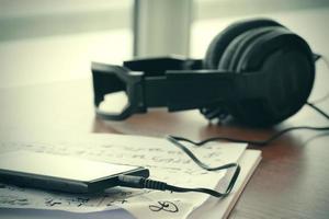 Closeup jack of smart phone with headphone on musical notes paper with shallow DOF evenly matched on wooden desk photo
