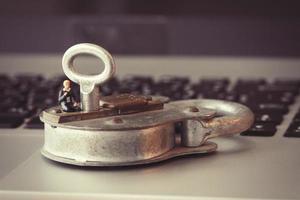 Internet security concept-miniature businessman stand on old key and padlock on laptop computer keyboard photo