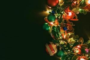 concepto de temporada de saludo corona de navidad con luz decorativa sobre fondo de madera oscura foto