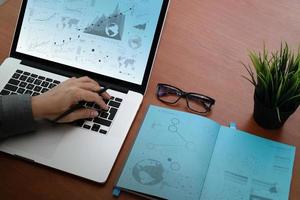 top view of businessman hand working with new modern blank screen computer on blank book on wooden desk with business strategy document and digital diagram as concept photo