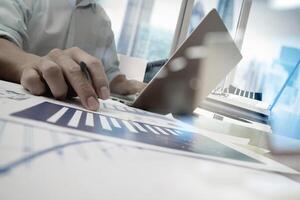 business documents on office table with smart phone and laptop computer and graph business with social network diagram and man working in the background photo