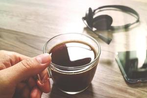 Hand holding Coffee cup or tea and voip headset,smart phone on wooden table,filter effect photo